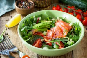 Healthy salad with quinoa, arugula, tomatoes, salmon and avocado on rustic table.