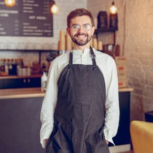 Cheerful male worker in apron standing in cafe