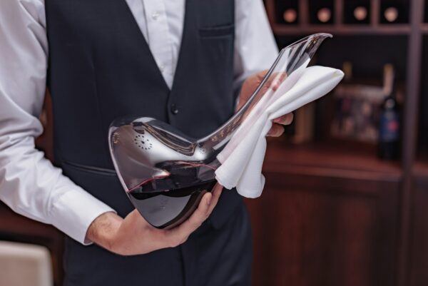 Cropped view man sommelier holding decanter with red wine in hands