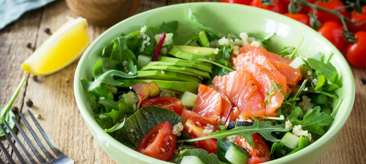 Healthy salad with quinoa, arugula, tomatoes, salmon and avocado on rustic table.